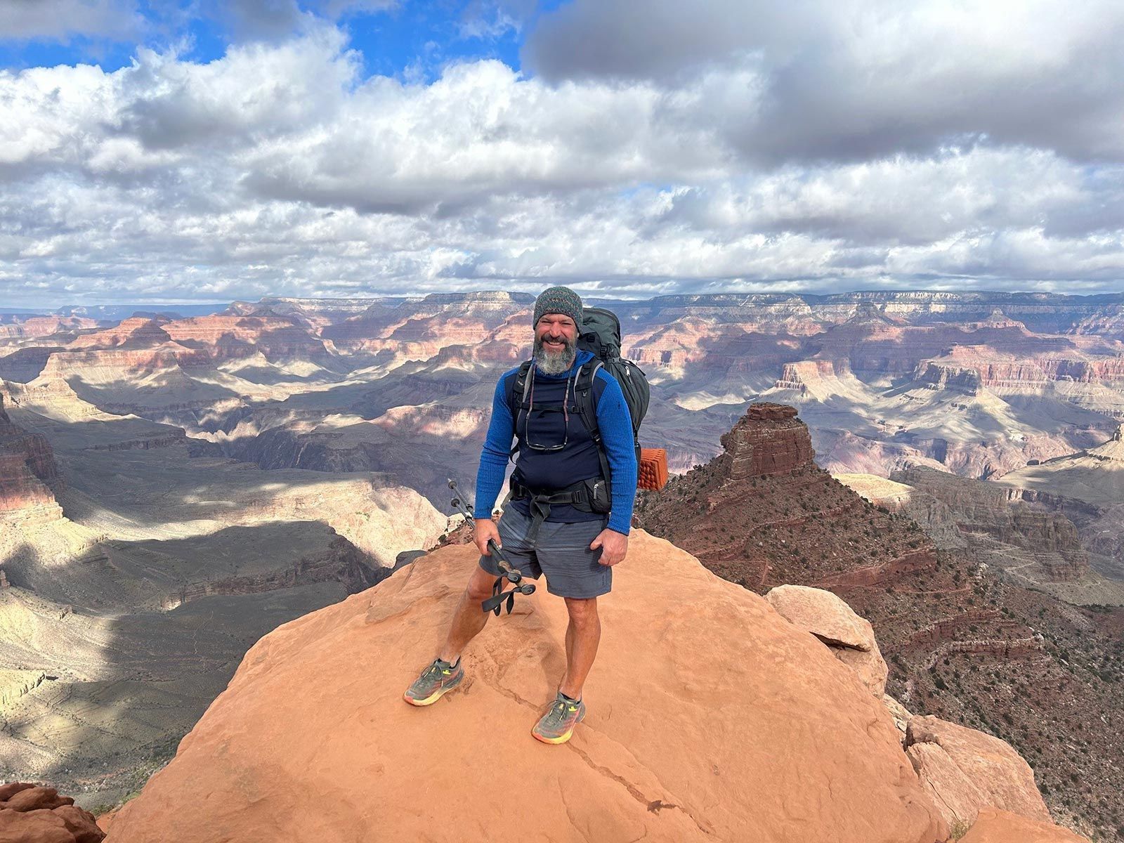 Hiker standing on a rocky overlook with a canyon backdrop and cloudy sky