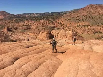 Two people are walking on a rocky hillside.