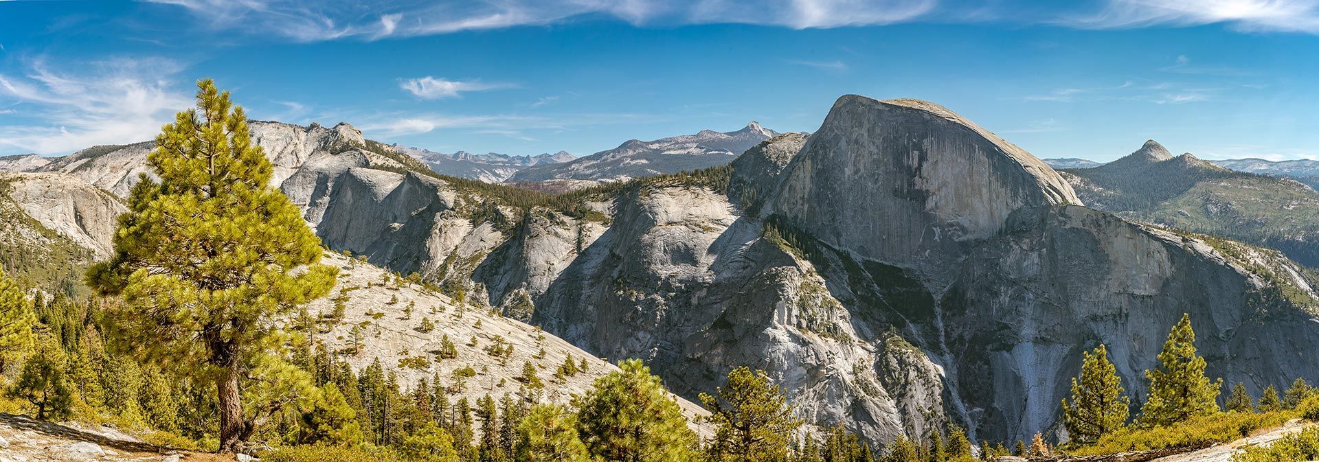 Mountain valley with granite cliffs, pine trees, and a blue sky with wispy clouds
