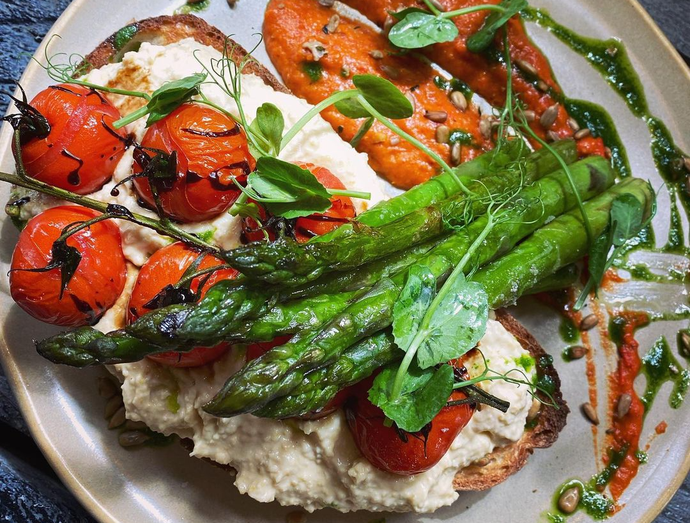 A plate of food with asparagus , tomatoes and hummus on toast.