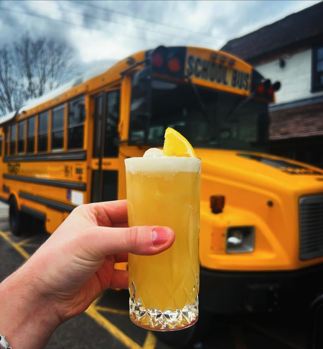 A person holding a cocktail in front of the notorious TOAST Bus