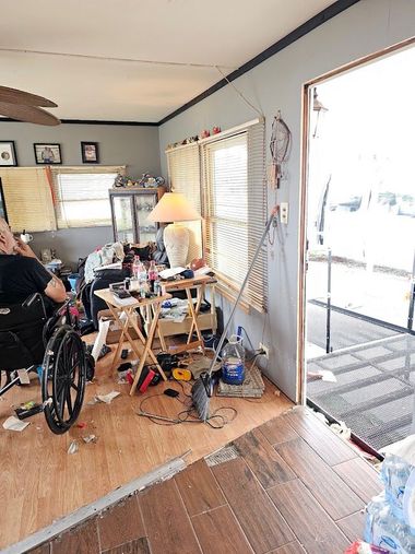 Cluttered living room with a wheelchair, table lamps, and an open door to a bright porch