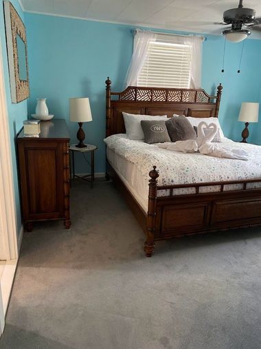 Blue bedroom with wooden bed, dresser, lamps, and a ceiling fan by a window with blinds.
