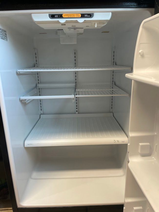 Open refrigerator with empty white shelves and drawers, interior light on.
