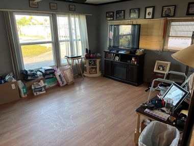 Bright living room with large windows, wood floor, and a TV stand against the wall.