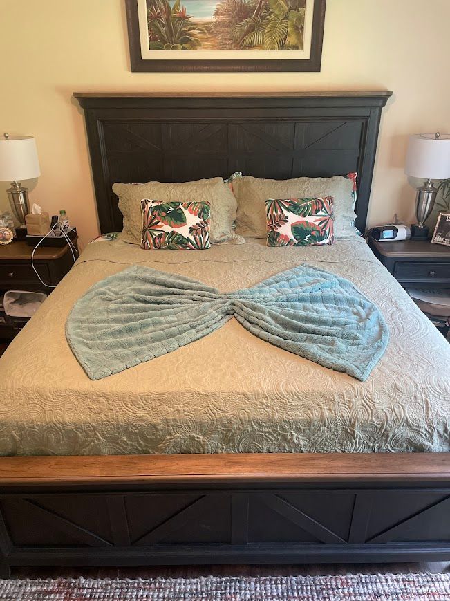 Neatly made bed with blue blanket, patterned pillows, dark wood headboard, and bedside lamps in a cozy bedroom.
