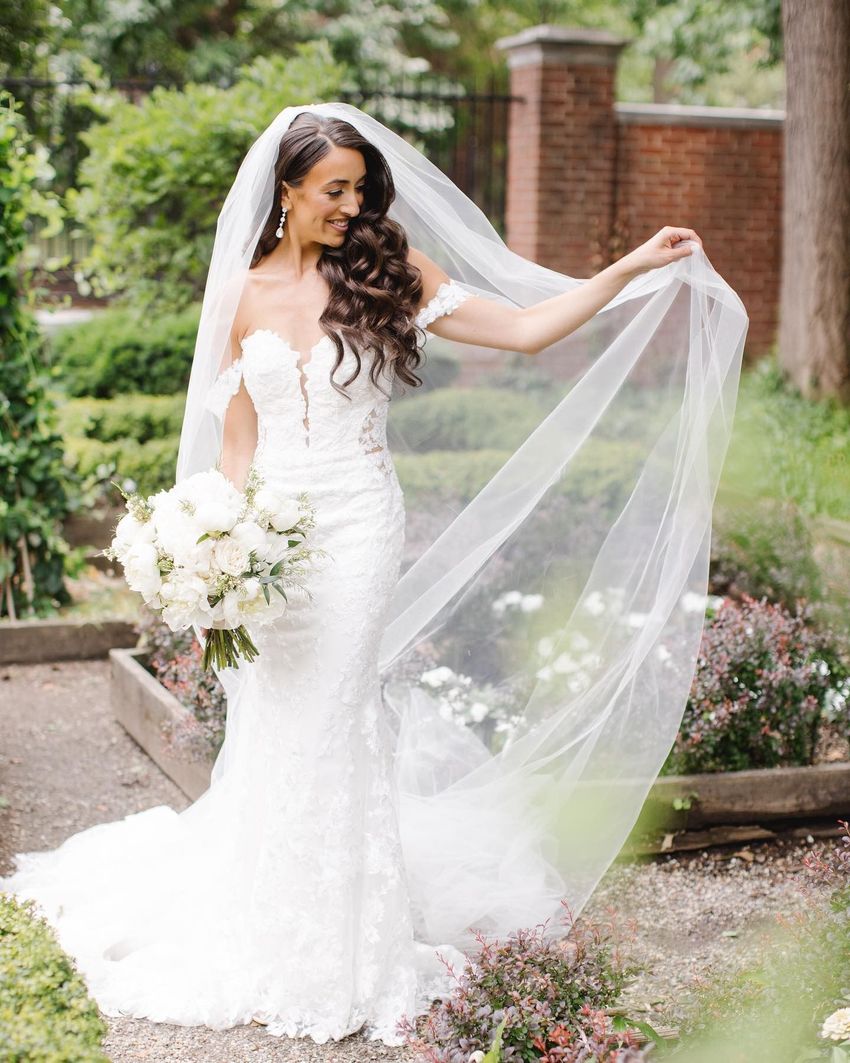 Bride in a white dress with veil, seated between two women in red dresses inside a rustic venue