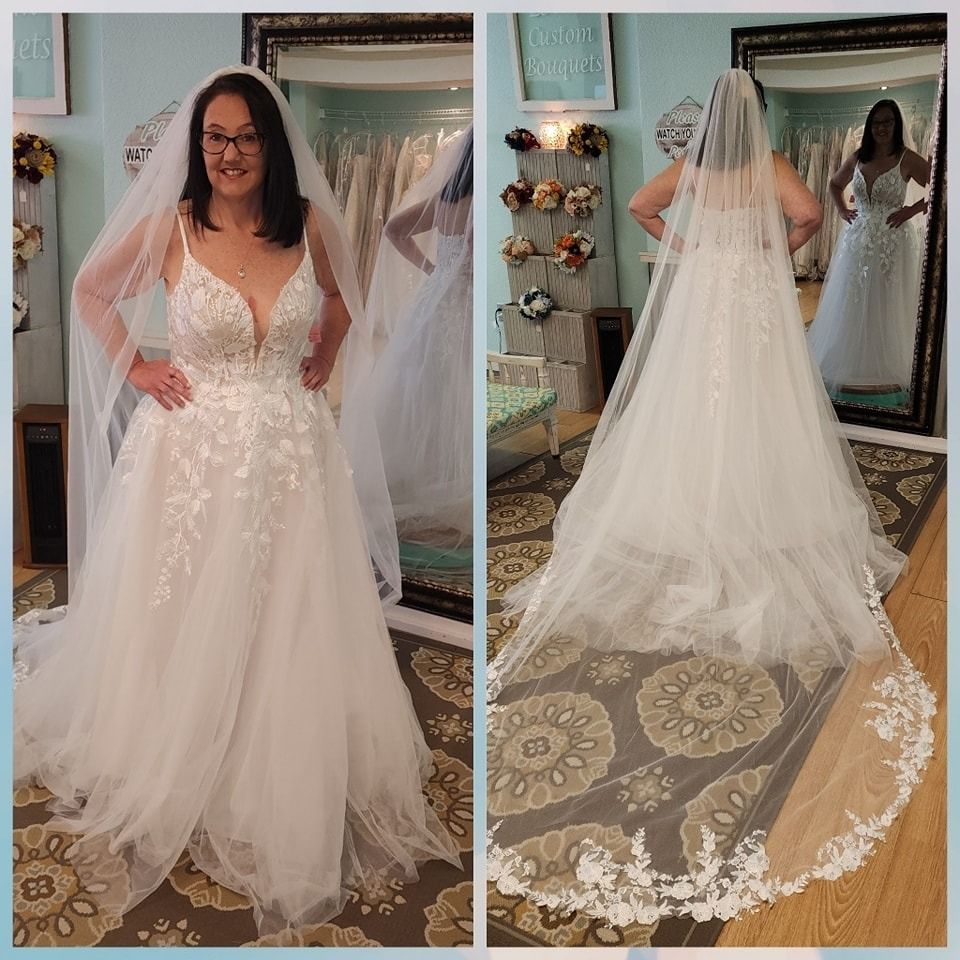 Bride modeling a white lace wedding gown with long veil, front and back views in a bridal shop