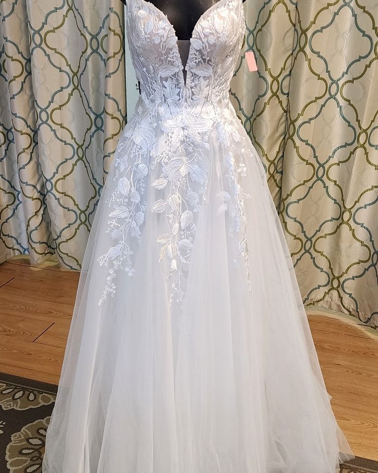 White strapless lace wedding dress with long tulle skirt displayed on a mannequin in a fitting room.