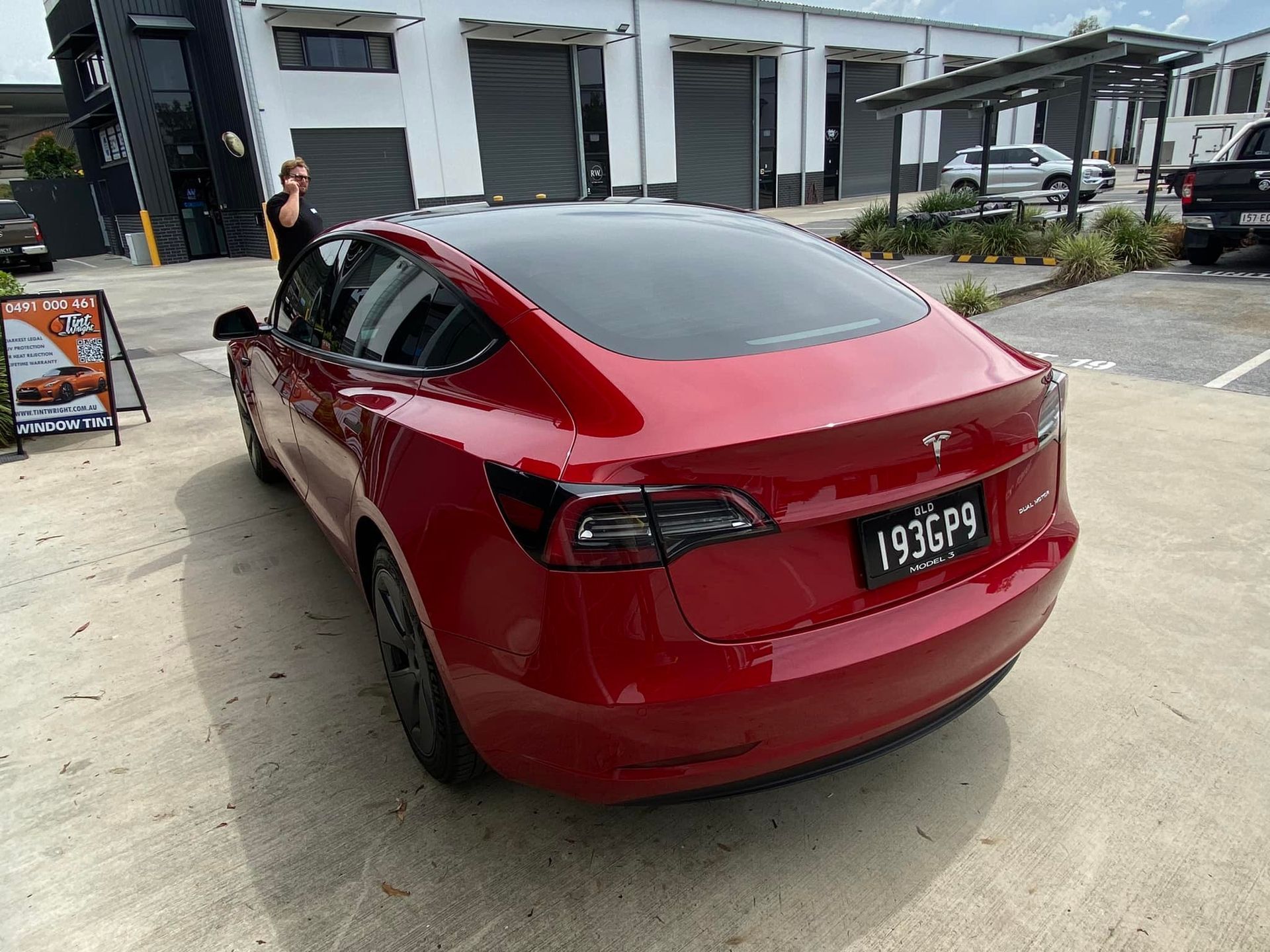 A red tesla model 3 is parked in a parking lot.