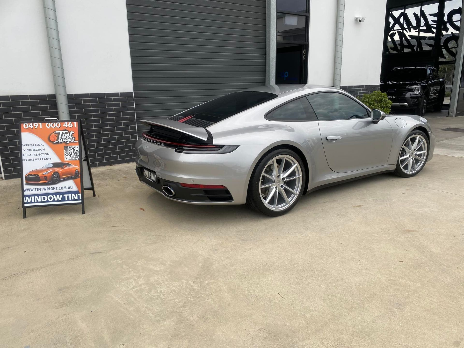 A silver porsche 911 is parked in front of a building.