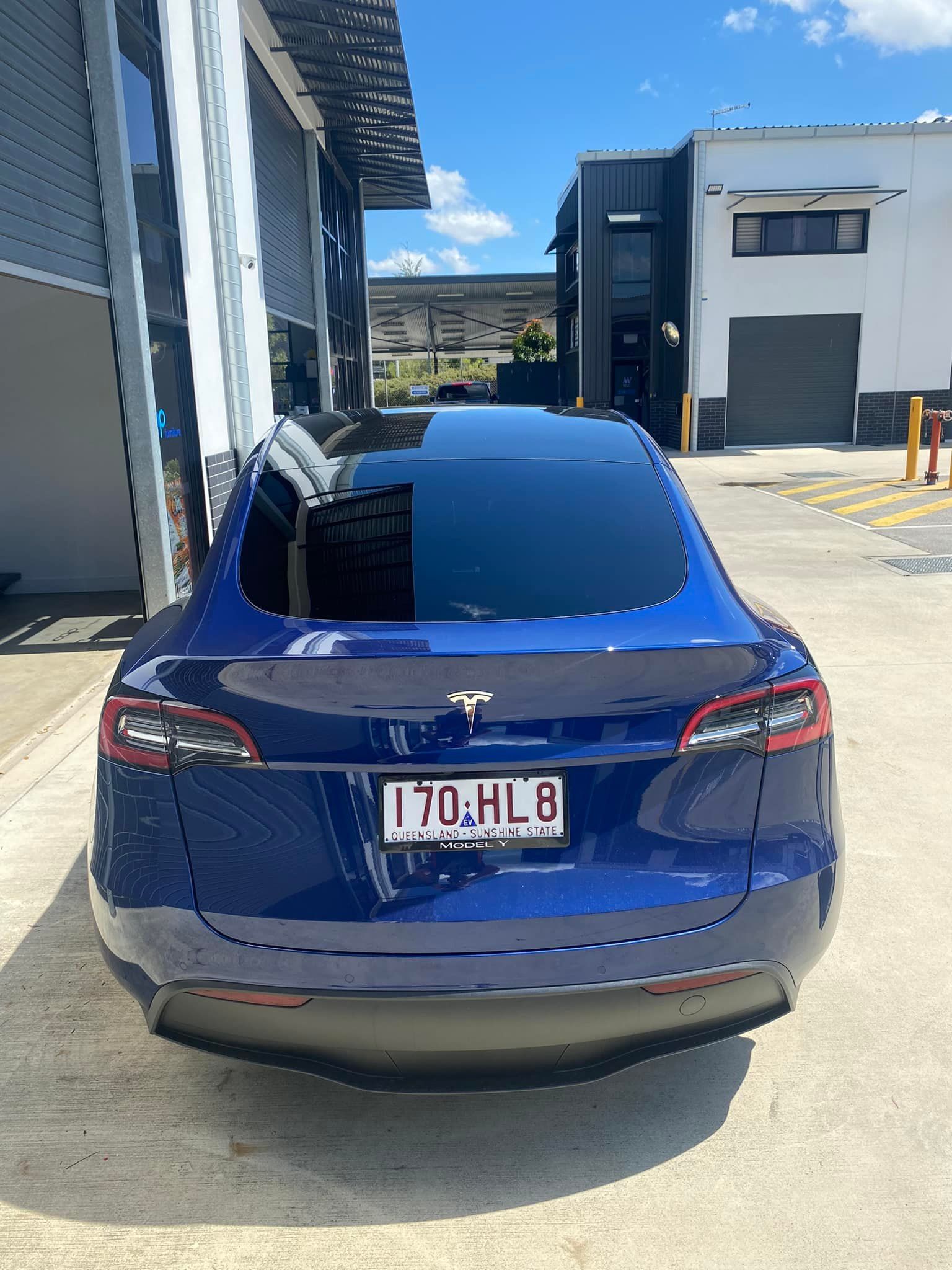 A blue tesla model 3 is parked in front of a building.