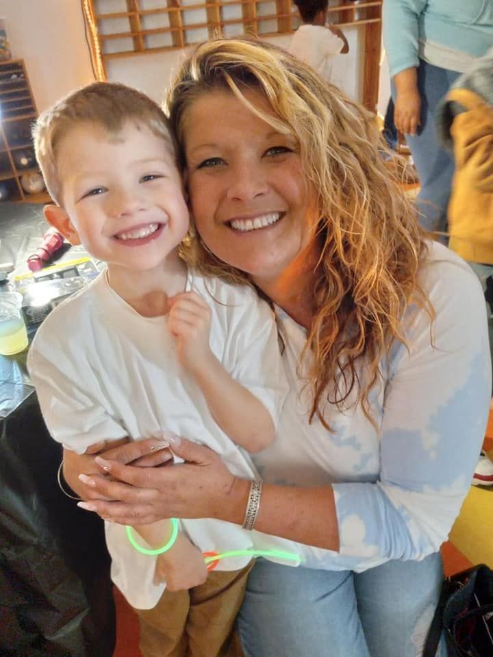 A smiling person embraces a young child, both wearing white shirts, in a casual indoor setting.