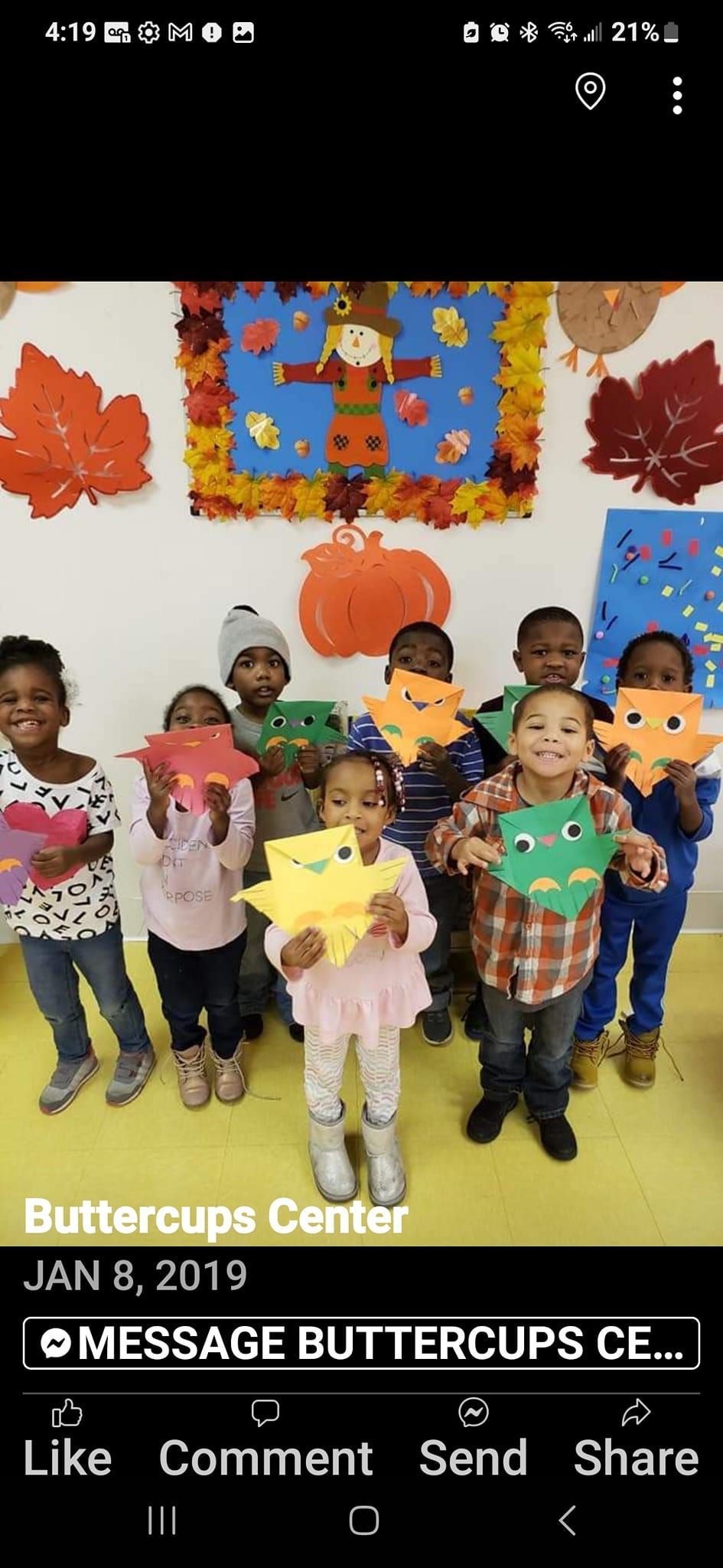 A group of children holding colorful paper leaves in a classroom decorated with seasonal fall wall art.