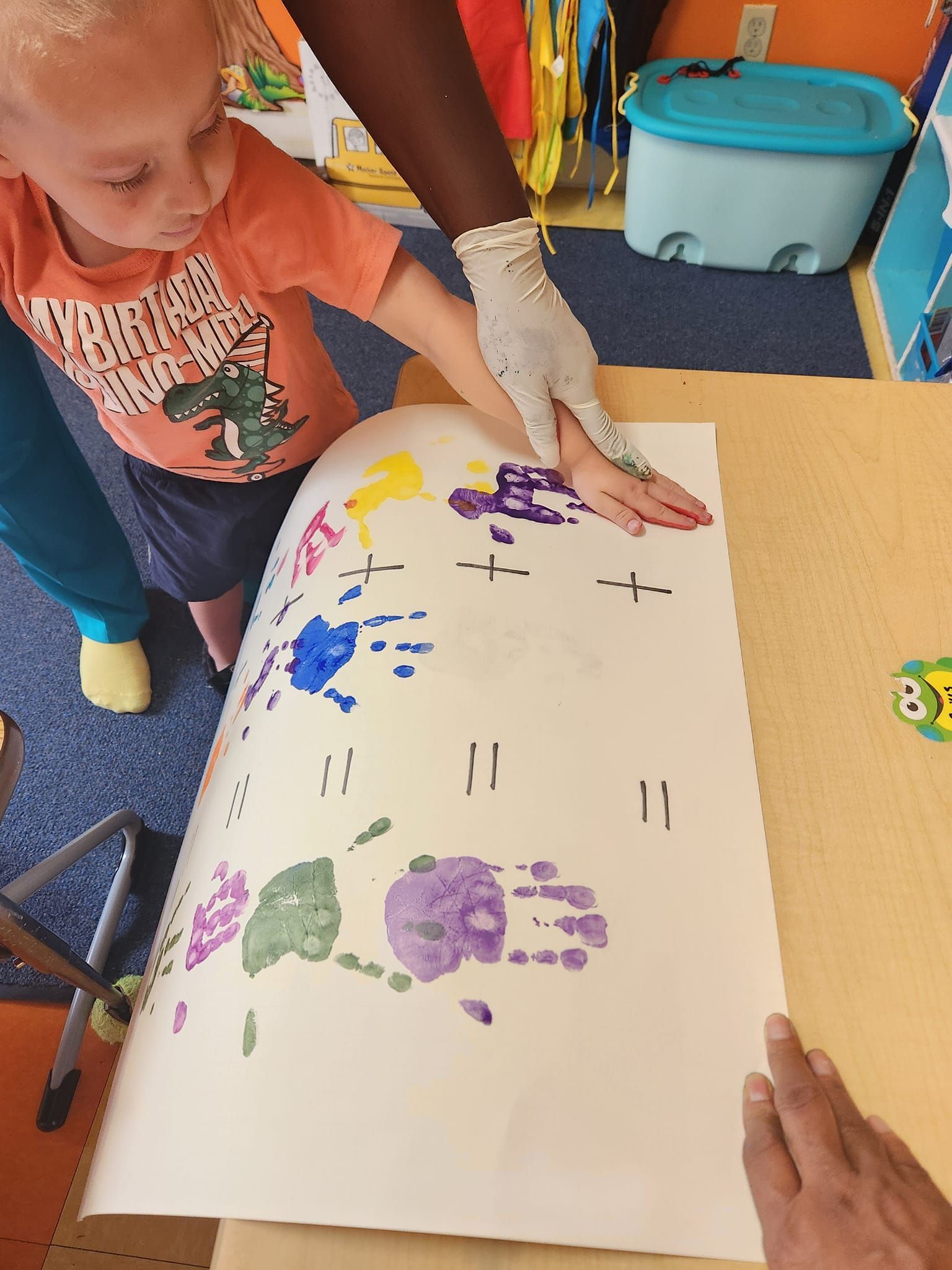 A child and adult use paint-covered hands to create colorful handprints on paper, forming an addition math worksheet.