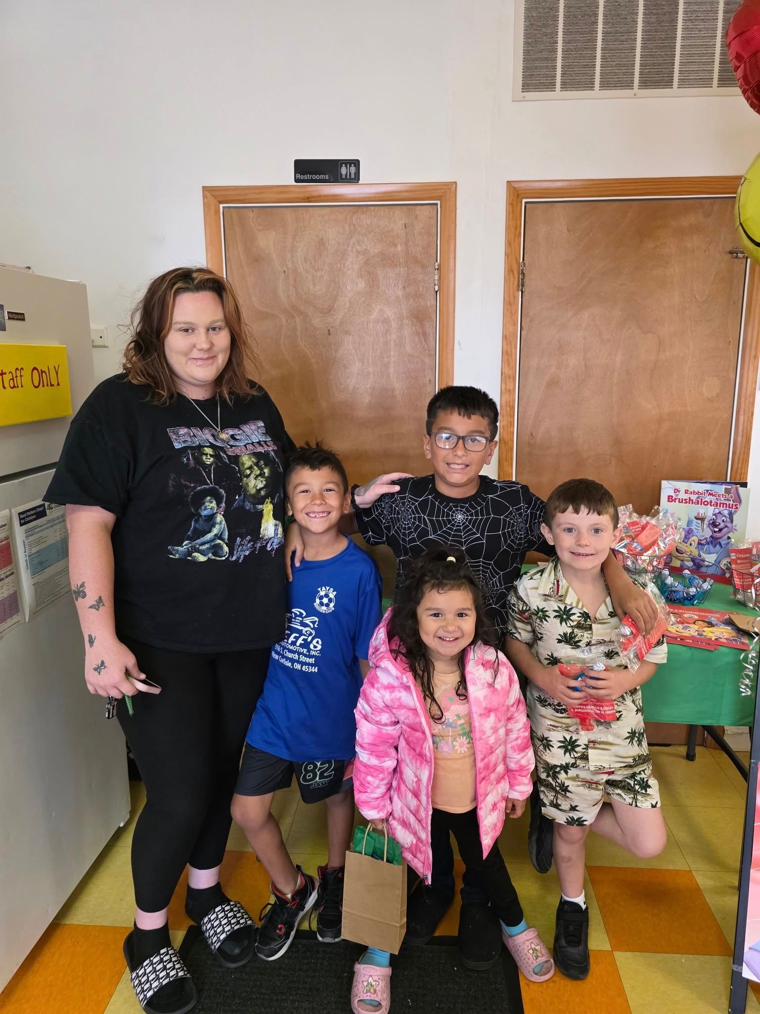 An adult and four children standing together indoors in a room with a green table and festive decorations.