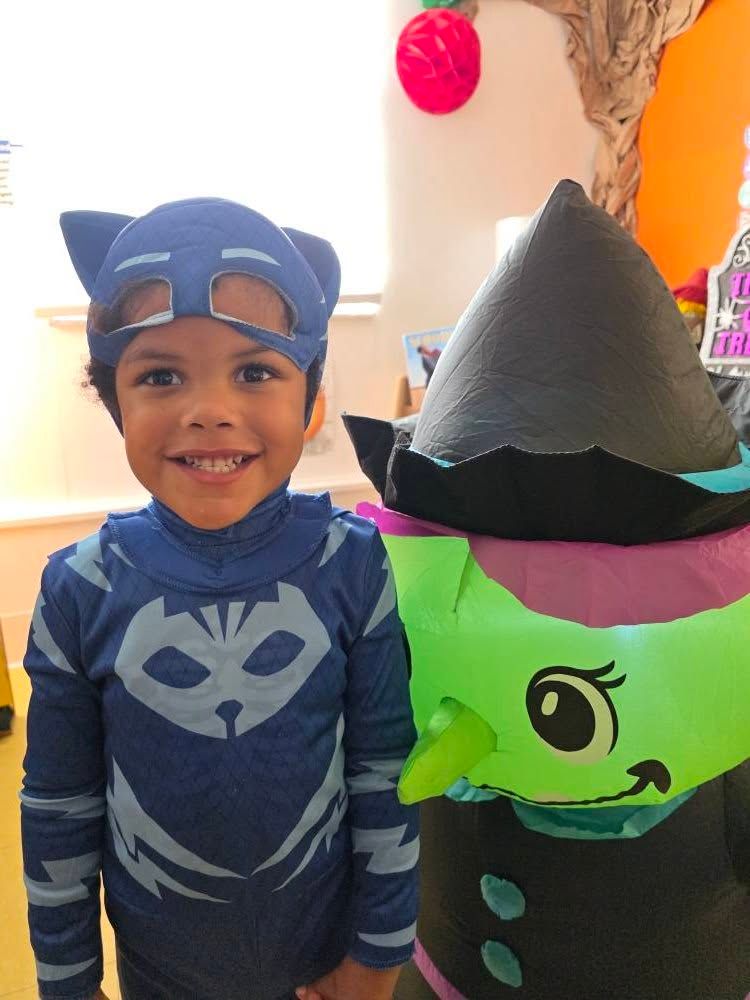 A child in a blue Catboy costume stands next to an inflatable green-faced witch.