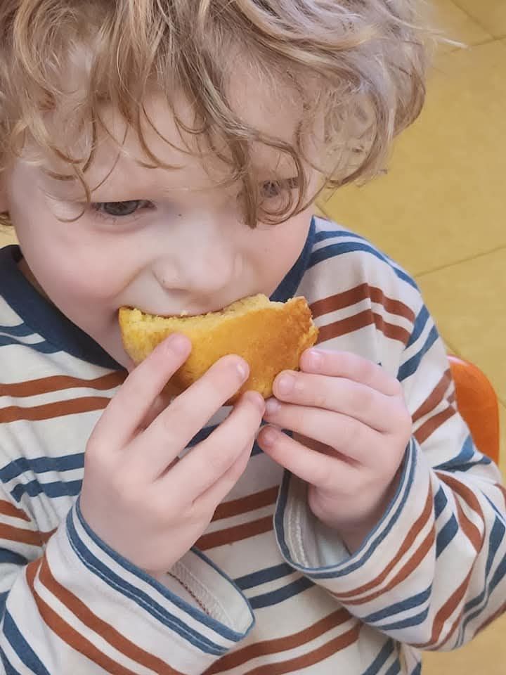 A person with curly hair wearing a striped shirt eats a piece of golden-yellow bread.