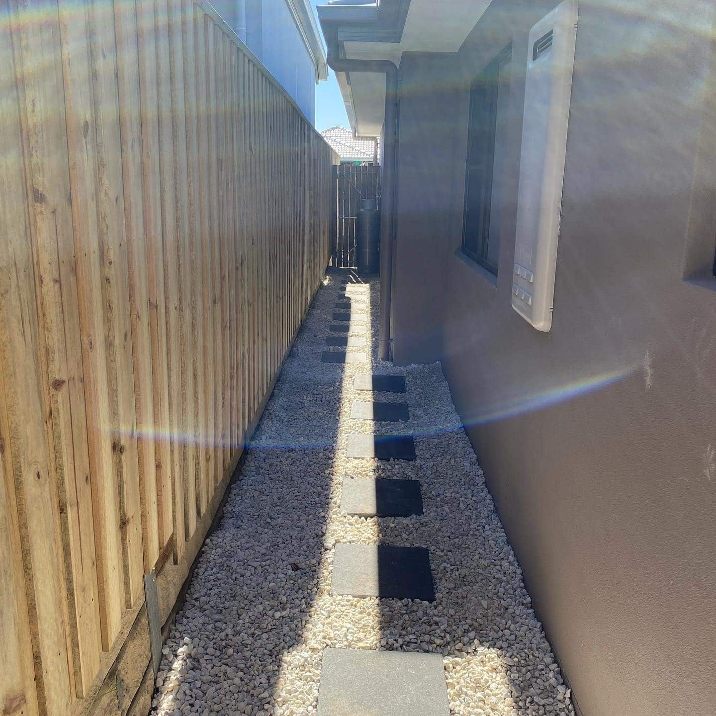 A narrow walkway between two houses with a wooden fence and gravel. — Turnscape Landscaping In Broadbeach, QLD