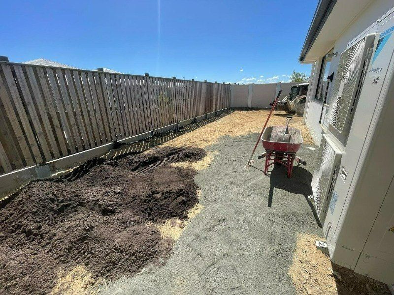 A Wheelbarrow is Sitting in a Backyard Next to a Fence  — Turnscape Landscaping in Hope Island, QLD