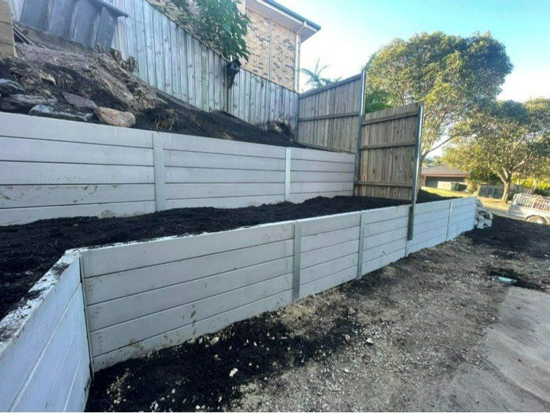 A White Retaining Wall With a Wooden Fence Behind It — Turnscape Landscaping In Broadbeach, QLD