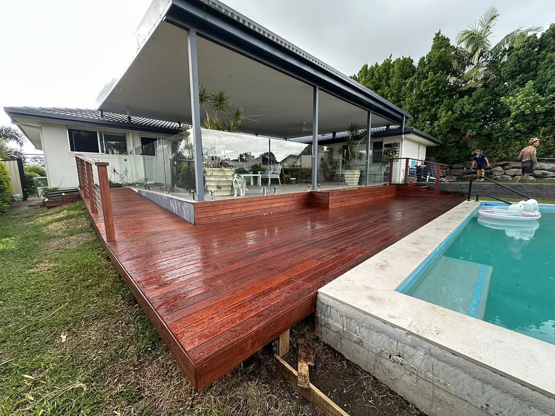 A wooden deck next to a swimming pool in front of a house. — Turnscape Landscaping in Robina, QLD
