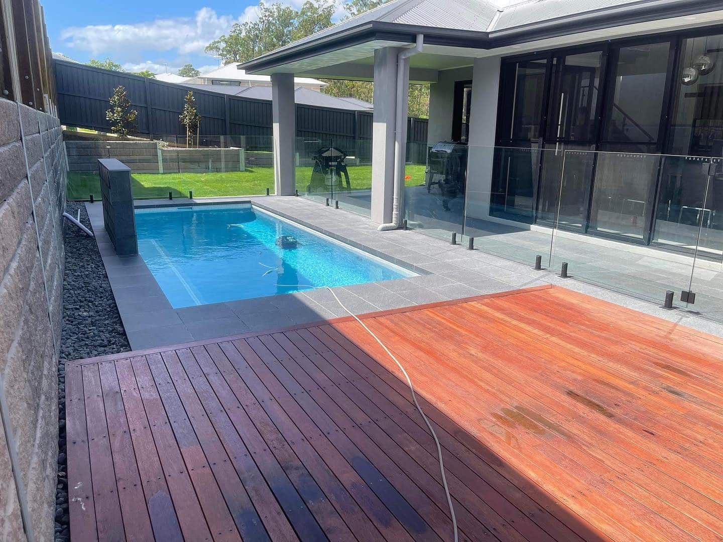There is a swimming pool in the backyard of a house with a wooden deck. — Turnscape Landscaping in Palm Beach, QLD