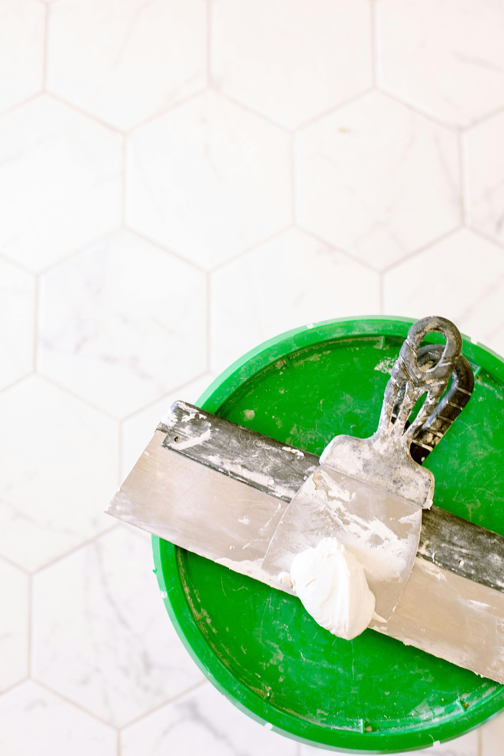 Two spatulas are sitting on top of a green bucket of plaster.