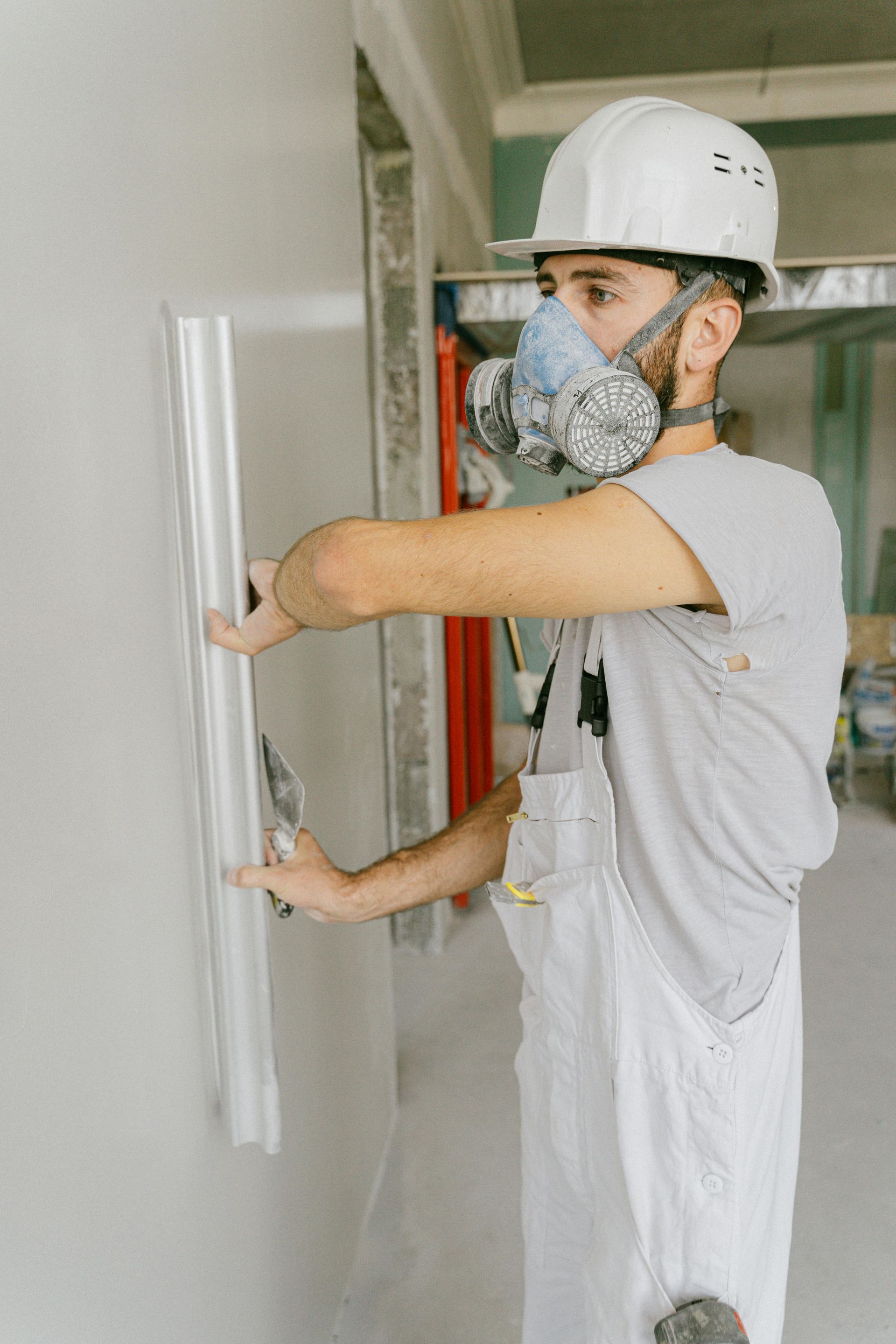 A man wearing a helmet and a gas mask is plastering a wall.