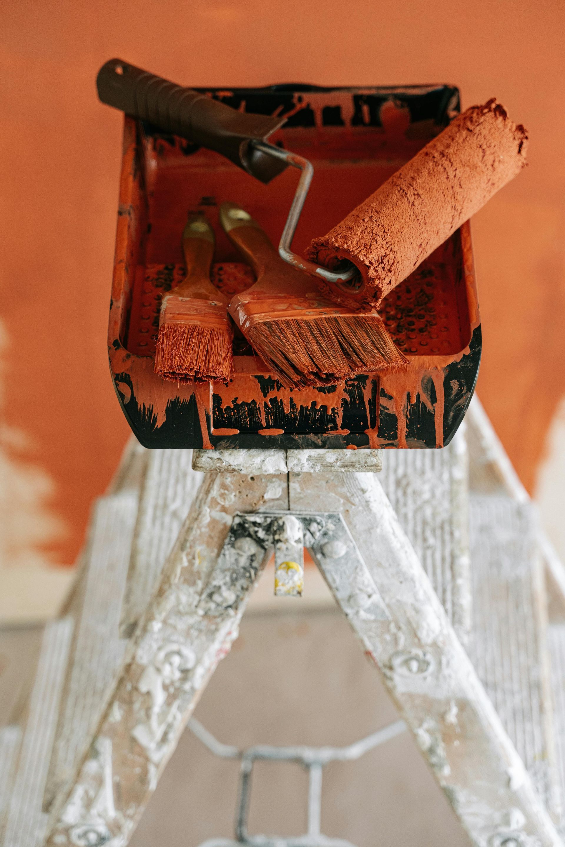 A ladder with paint rollers and brushes on it.