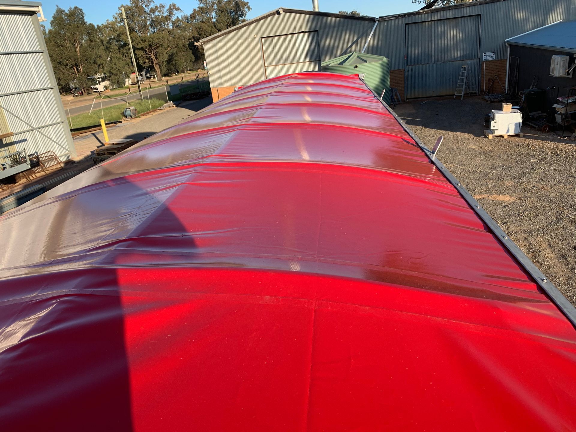 Red tarp roof stretching across an outdoor structure, with sheds and a yard in the background.