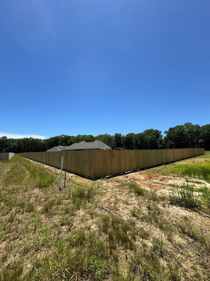 Vacant grassy lot with a wooden privacy fence under a clear blue sky