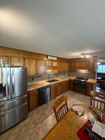 Wooden kitchen with stainless steel appliances, tan tile floor, and dining table in foreground