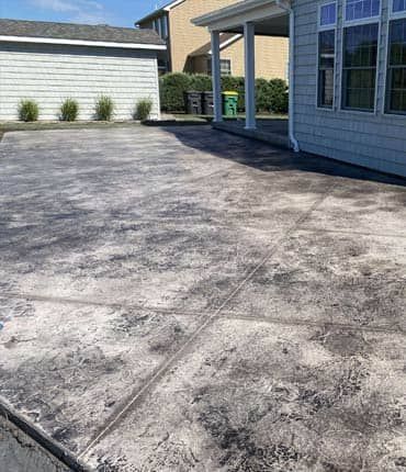 Stamped concrete patio with a mottled gray and white finish next to a light blue house.