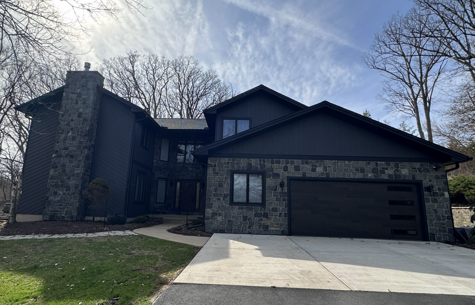 Modern dark-brick house with a two-car garage and bare trees in front
