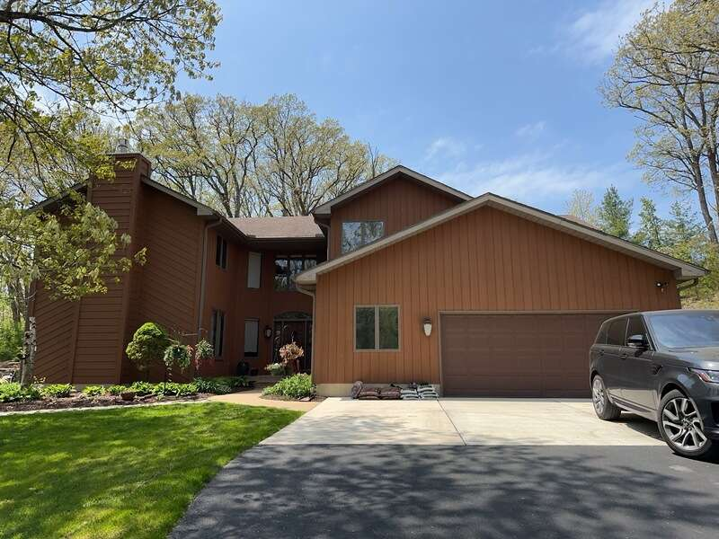 Suburban house with brown siding, driveway, green lawn, and parked SUV under a blue sky