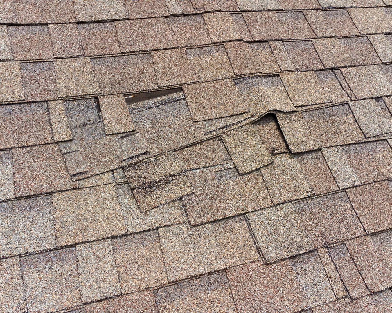 Damaged asphalt roof shingles with cracks, lifting tabs, and patches of wear