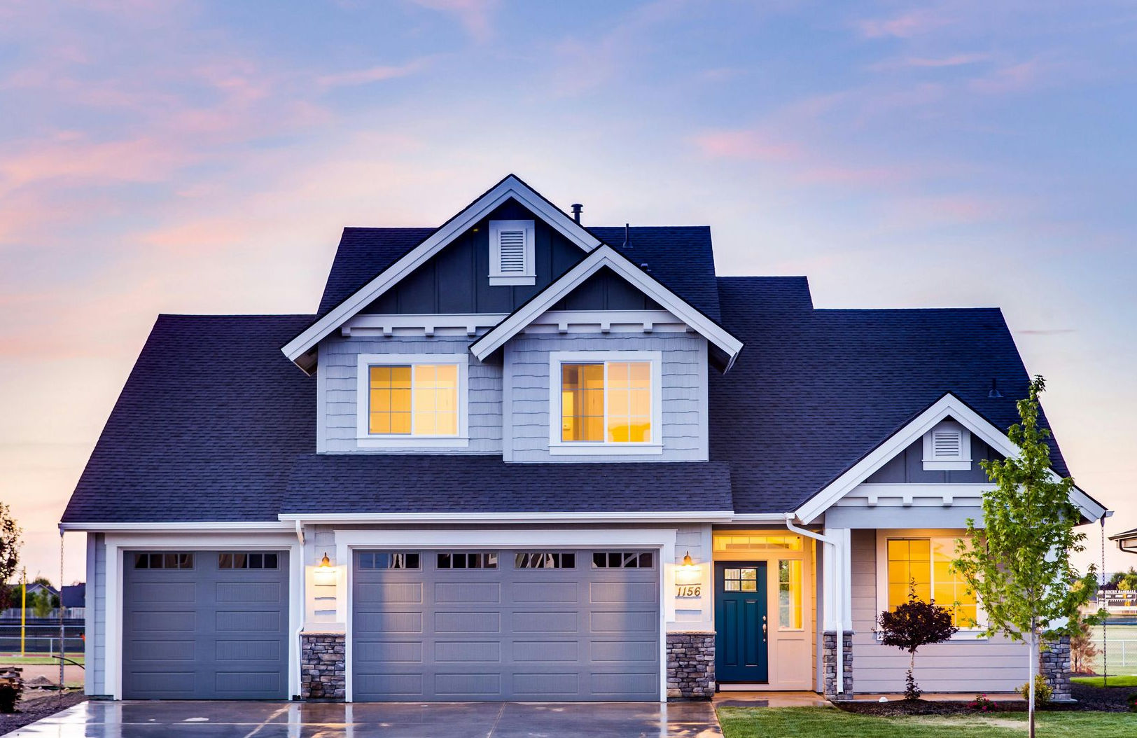 Suburban two-story gray house with lit windows and double garage at sunset