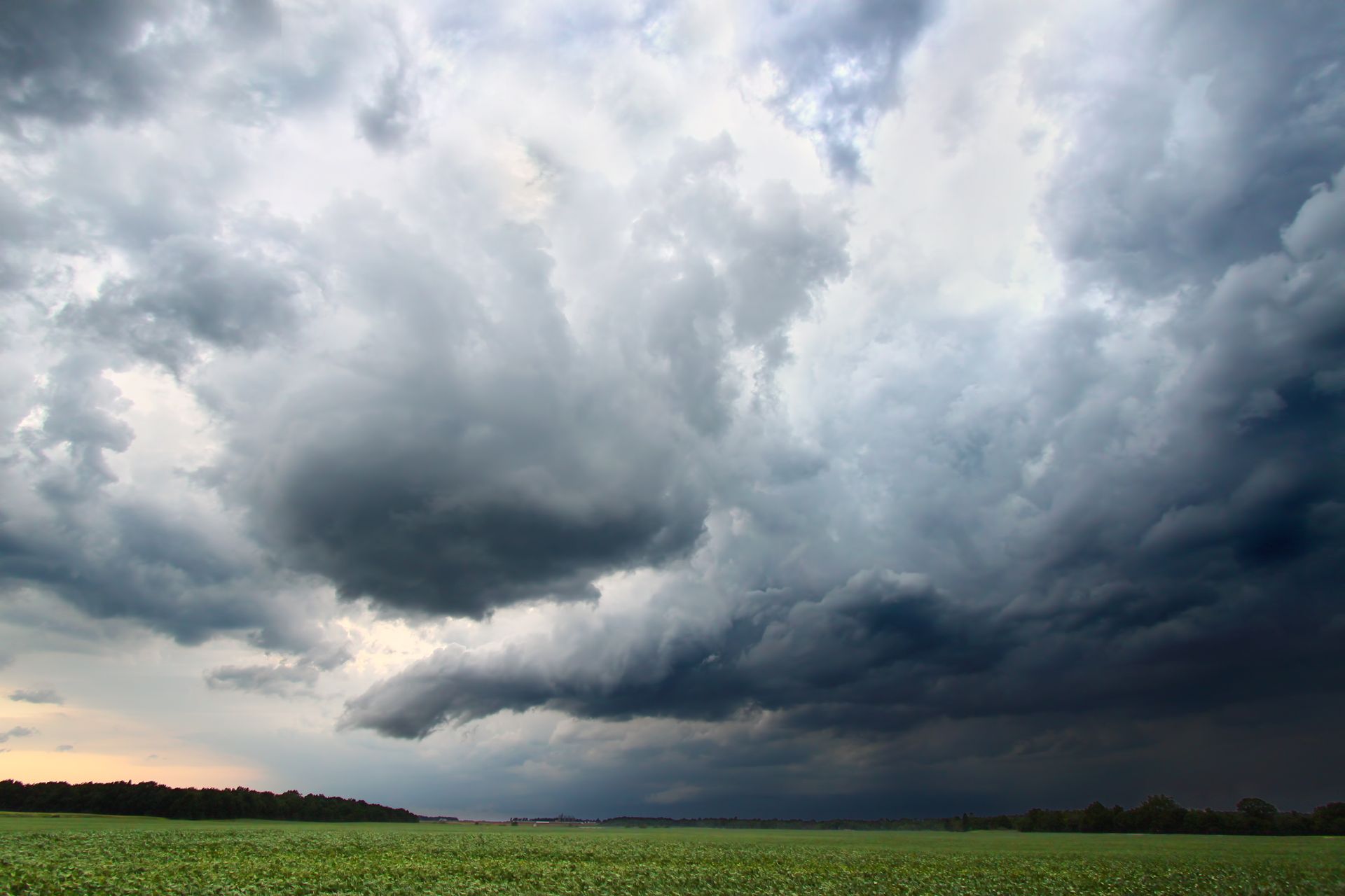 Dark storm clouds over a green field at sunset