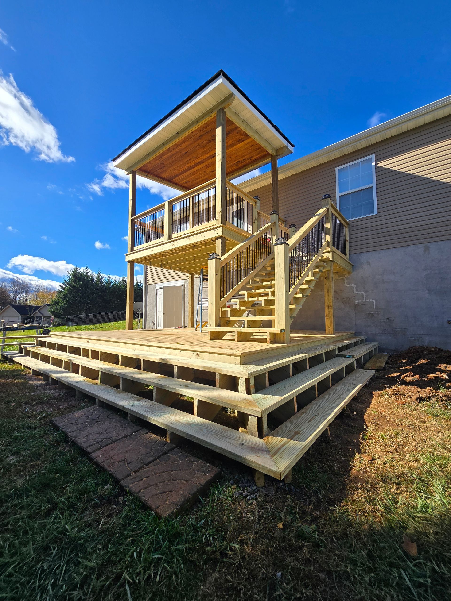A wooden deck with stairs leading up to it is in the backyard of a house.