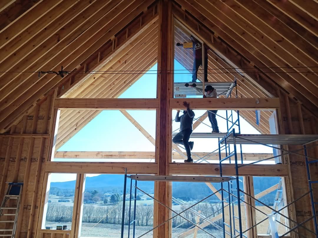 A man is standing on a scaffolding in a room with a large window.