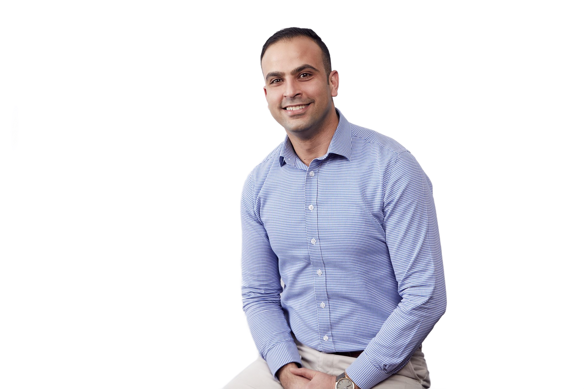 Man seated on a white background, wearing a blue patterned shirt and smiling.