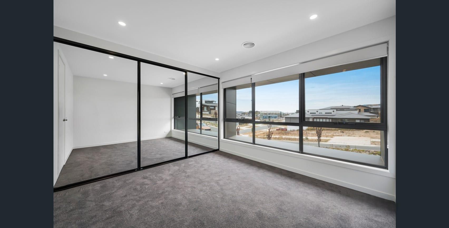 Empty modern apartment room with gray carpet, black-framed sliding doors, and large windows overlooking city views