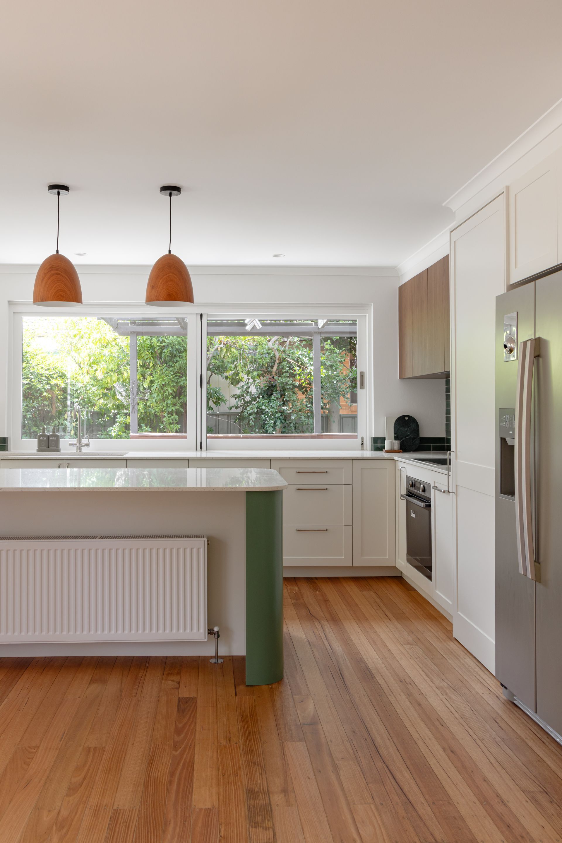 Bright modern kitchen with white cabinets, island, wooden floor, pendant lights, and stainless refrigerator