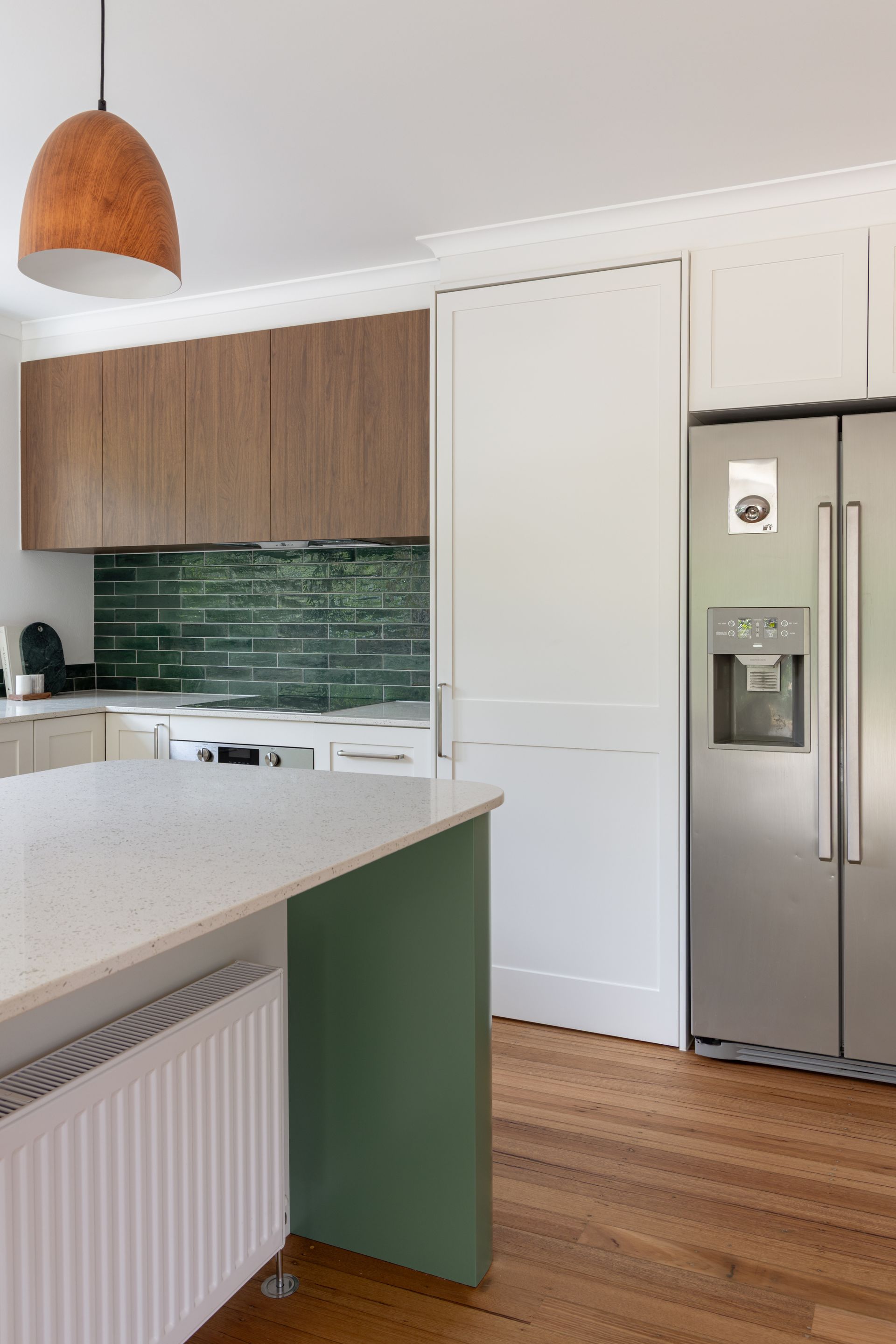 Modern kitchen with white cabinets, wood accents, green tile backsplash, and stainless steel refrigerator