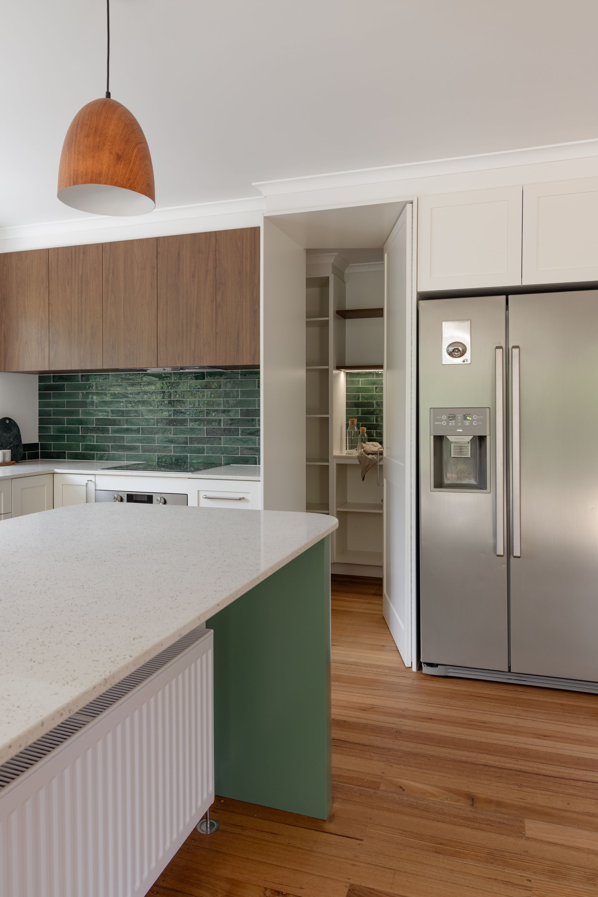 Modern kitchen with white island, wood cabinets, green backsplash, and stainless steel refrigerator