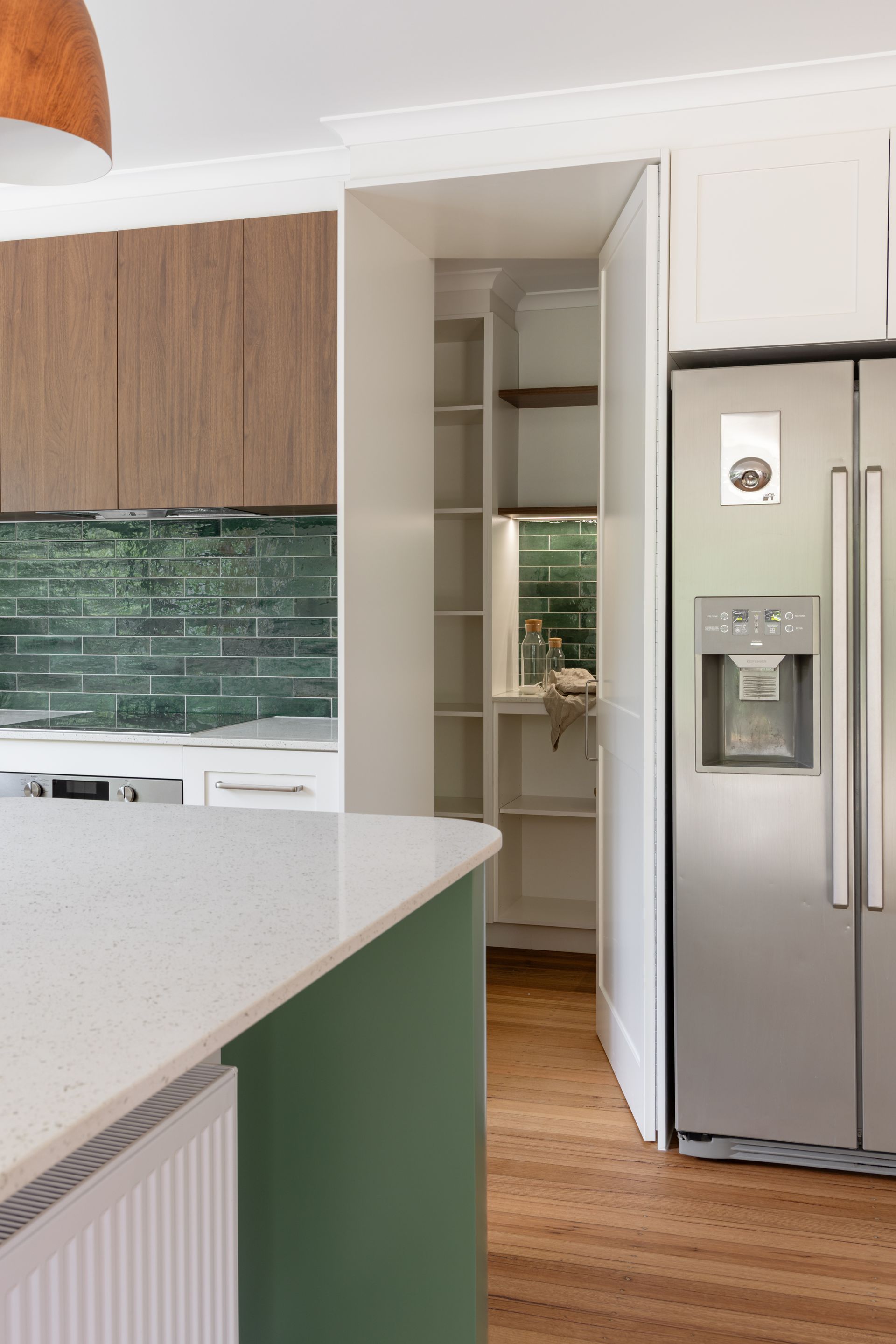 Modern kitchen with white cabinets, green backsplash, stainless fridge, and a narrow pantry opening