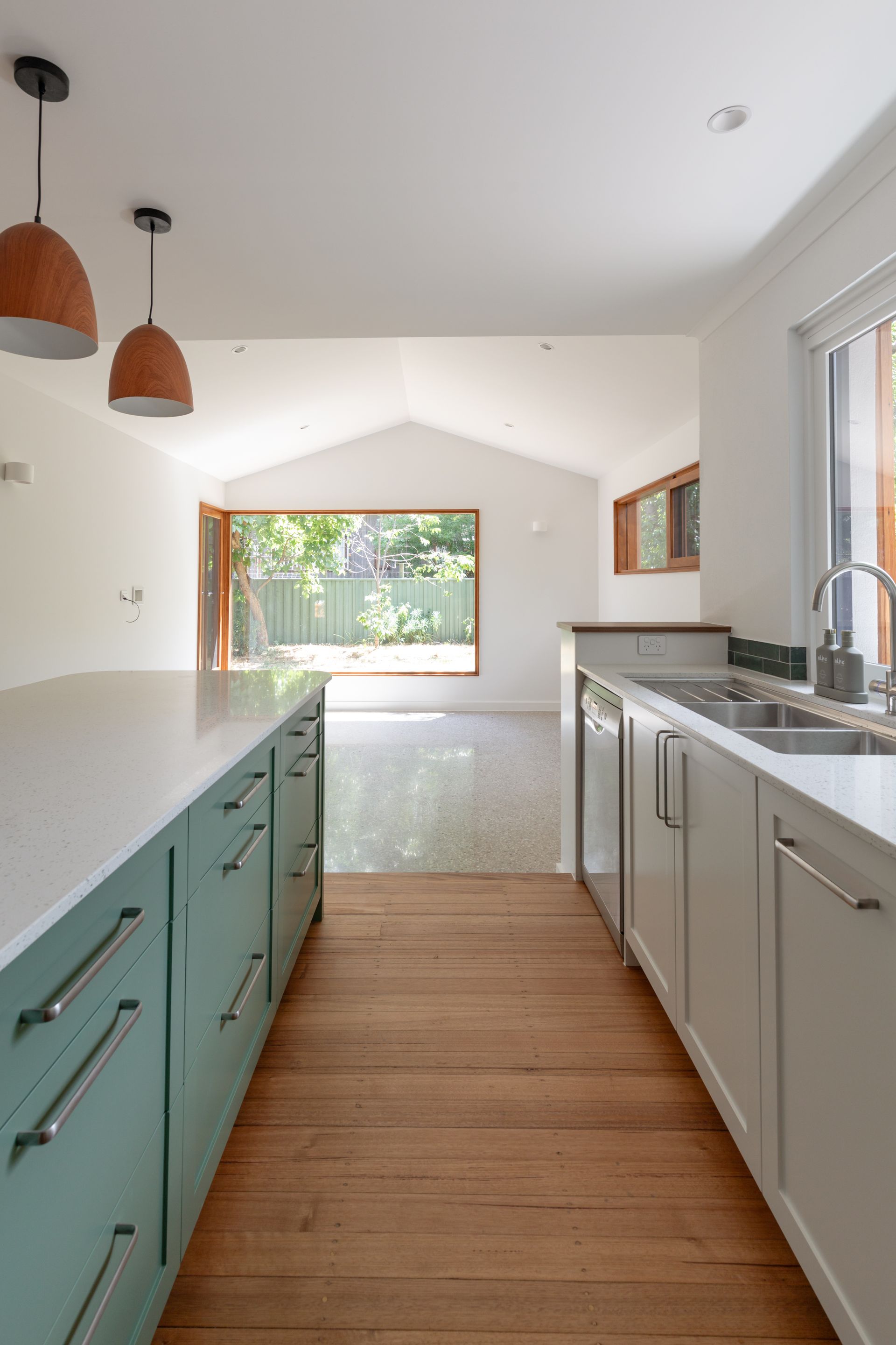 Bright modern kitchen with teal and white cabinets, wood floor, and a large window view of greenery.