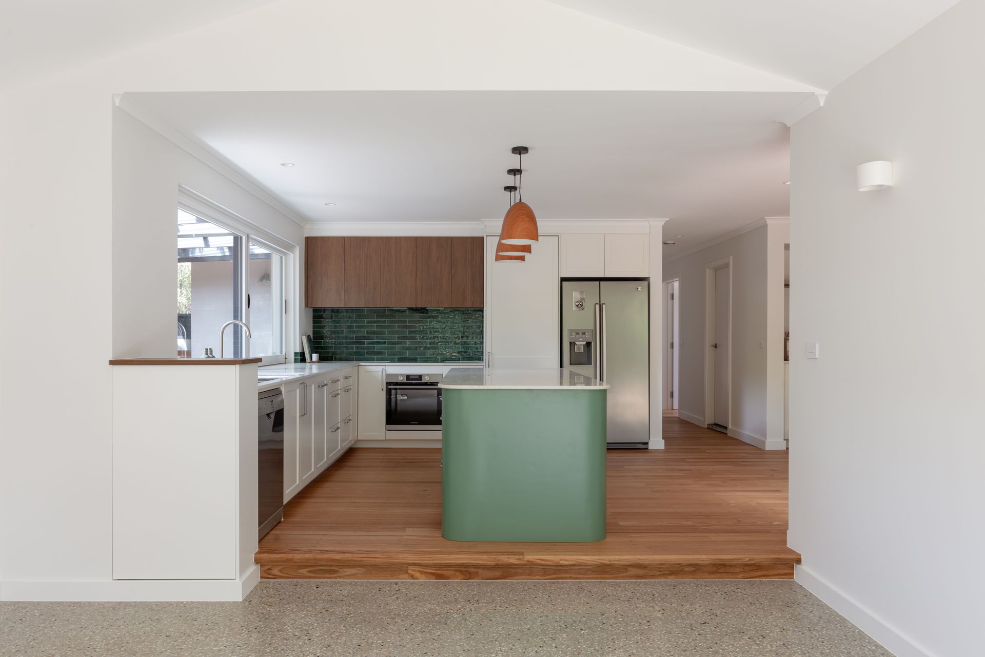 Open-plan kitchen with white walls, wood floors, green island, and orange pendant light