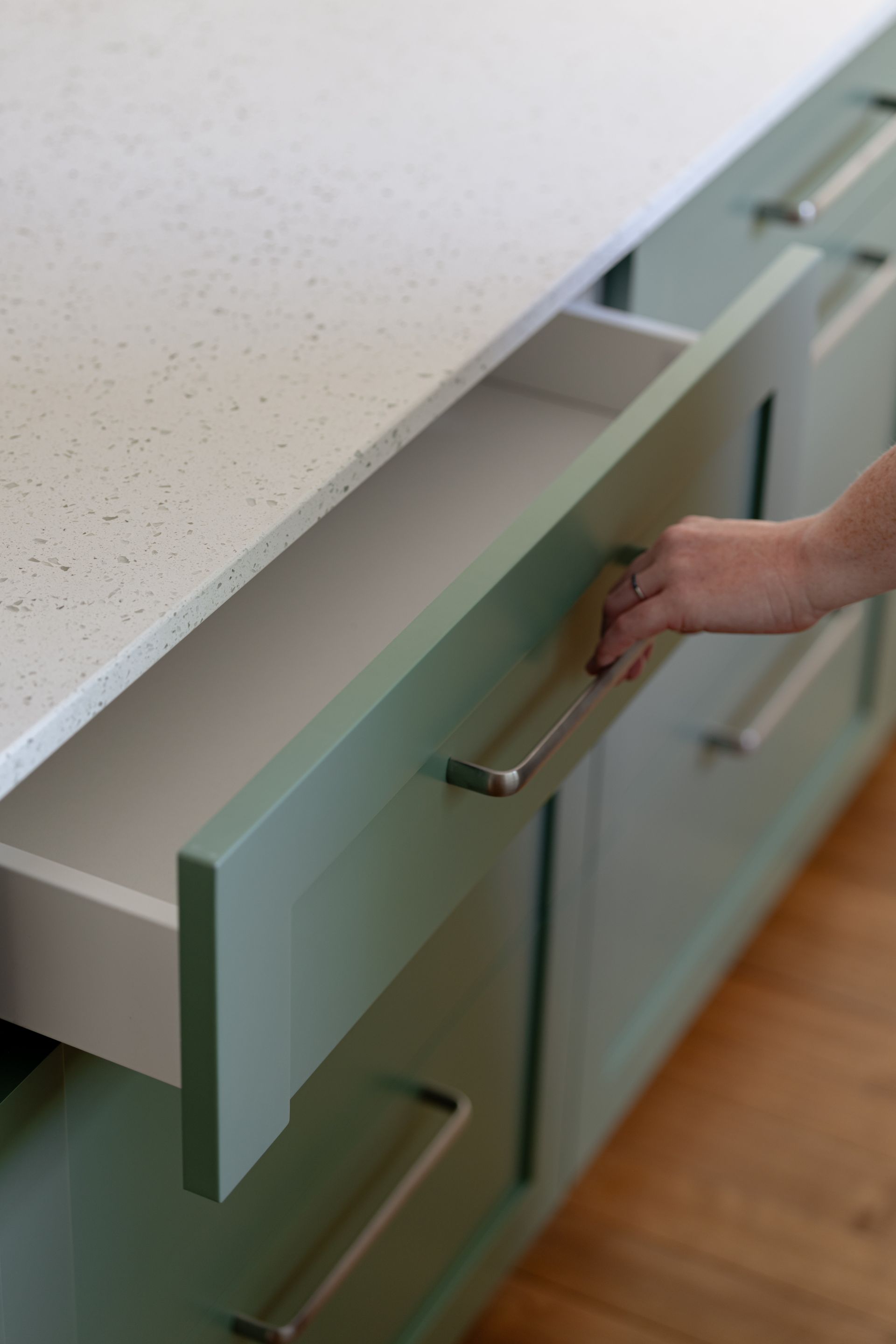 Hand opening a mint-green kitchen cabinet drawer beside a white countertop